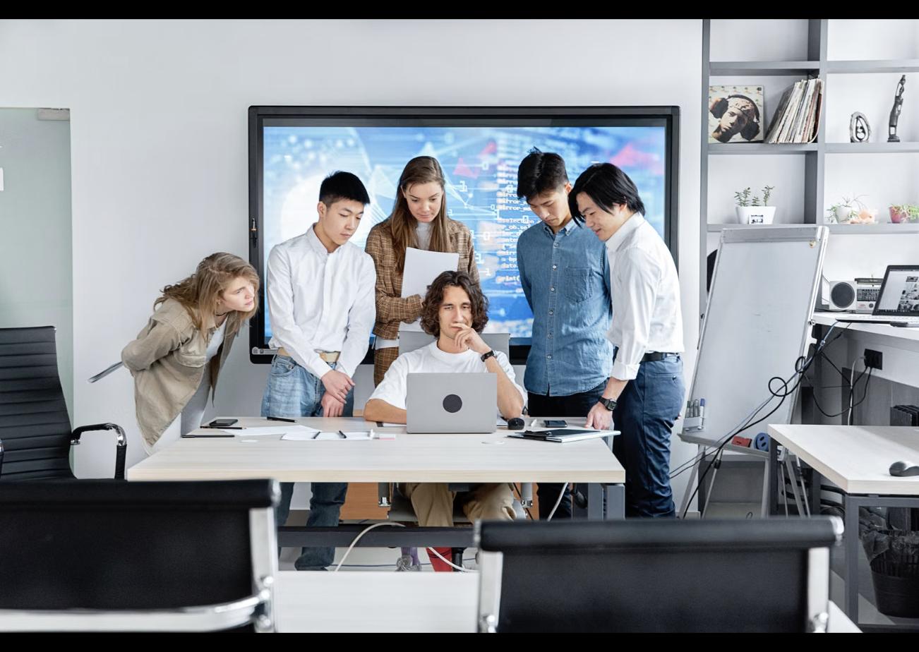 Product team collaborating around a laptop, discussing in-house hiring versus a dedicated product studio in Singapore